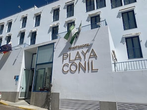 Un edificio con un letrero que dice 'APARTHOTEL PLAYA CONIL' y una bandera.