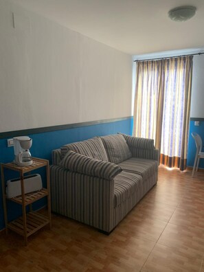 A room with a striped sofa, a coffee maker, and a toaster on a wooden shelf. - Apartahotel Playa Conil (Conil de la Frontera)
