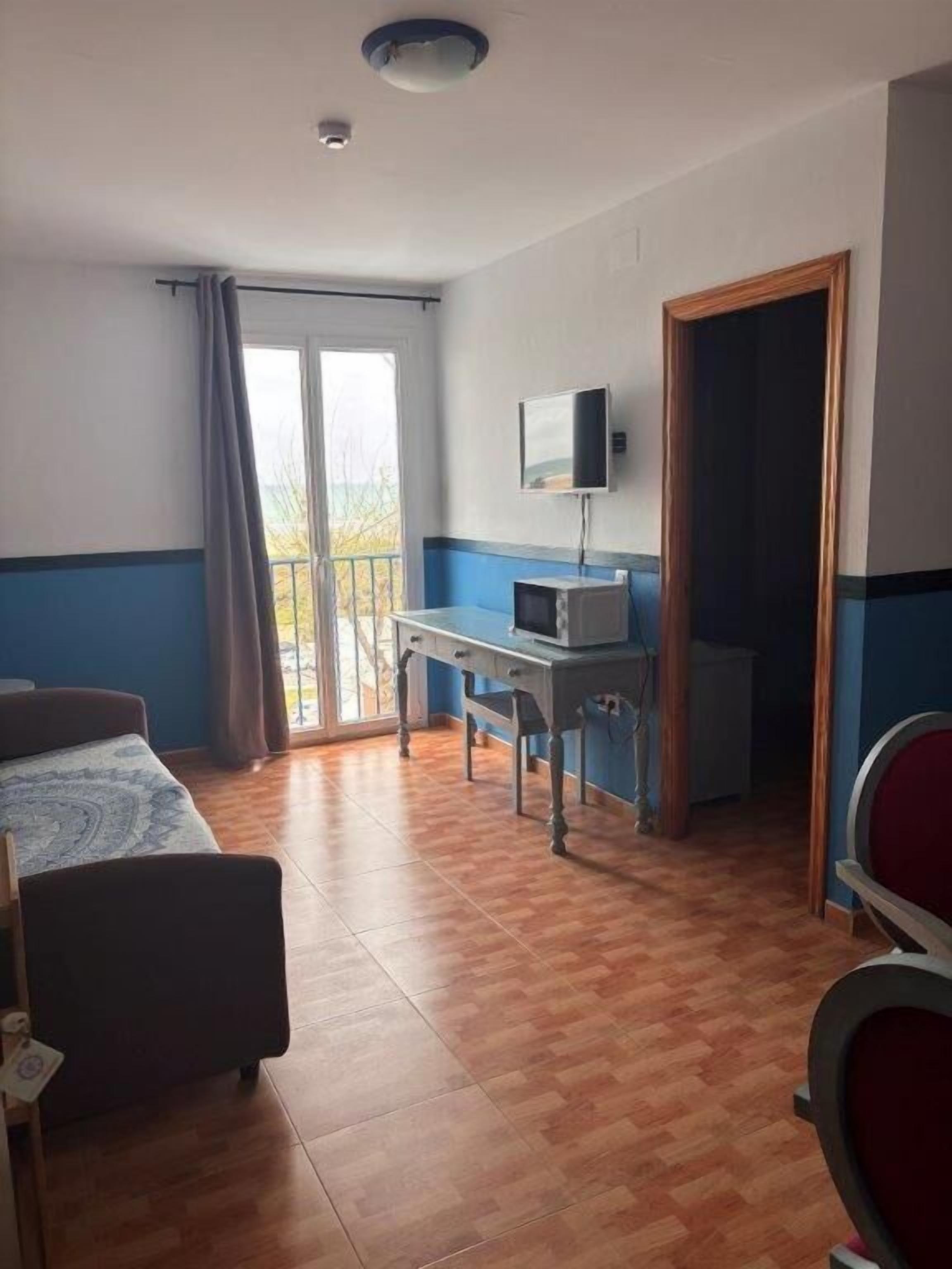 Habitació d'hotel amb llit, escriptori amb ordinador, televisió i balcó amb cortines.