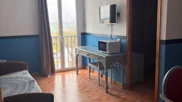 Habitació d'hotel amb llit, escriptori amb ordinador, televisió i balcó amb cortines.