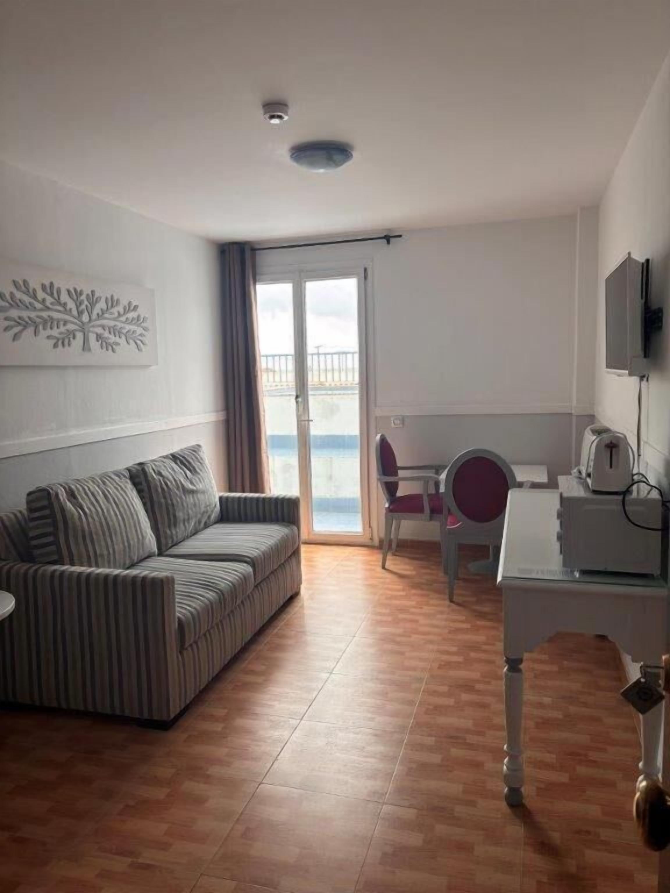 Habitació amb un sofà estriat, un escriptori amb una cadira, una televisió i una vista per una porta de vidre.