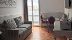A room with a striped sofa, a desk with a chair, a television, and a view through a glass door. - Apartahotel Playa Conil (Conil de la Frontera)