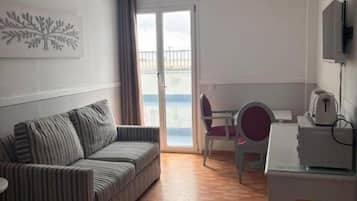 Habitació amb un sofà estriat, un escriptori amb una cadira, una televisió i una vista per una porta de vidre.