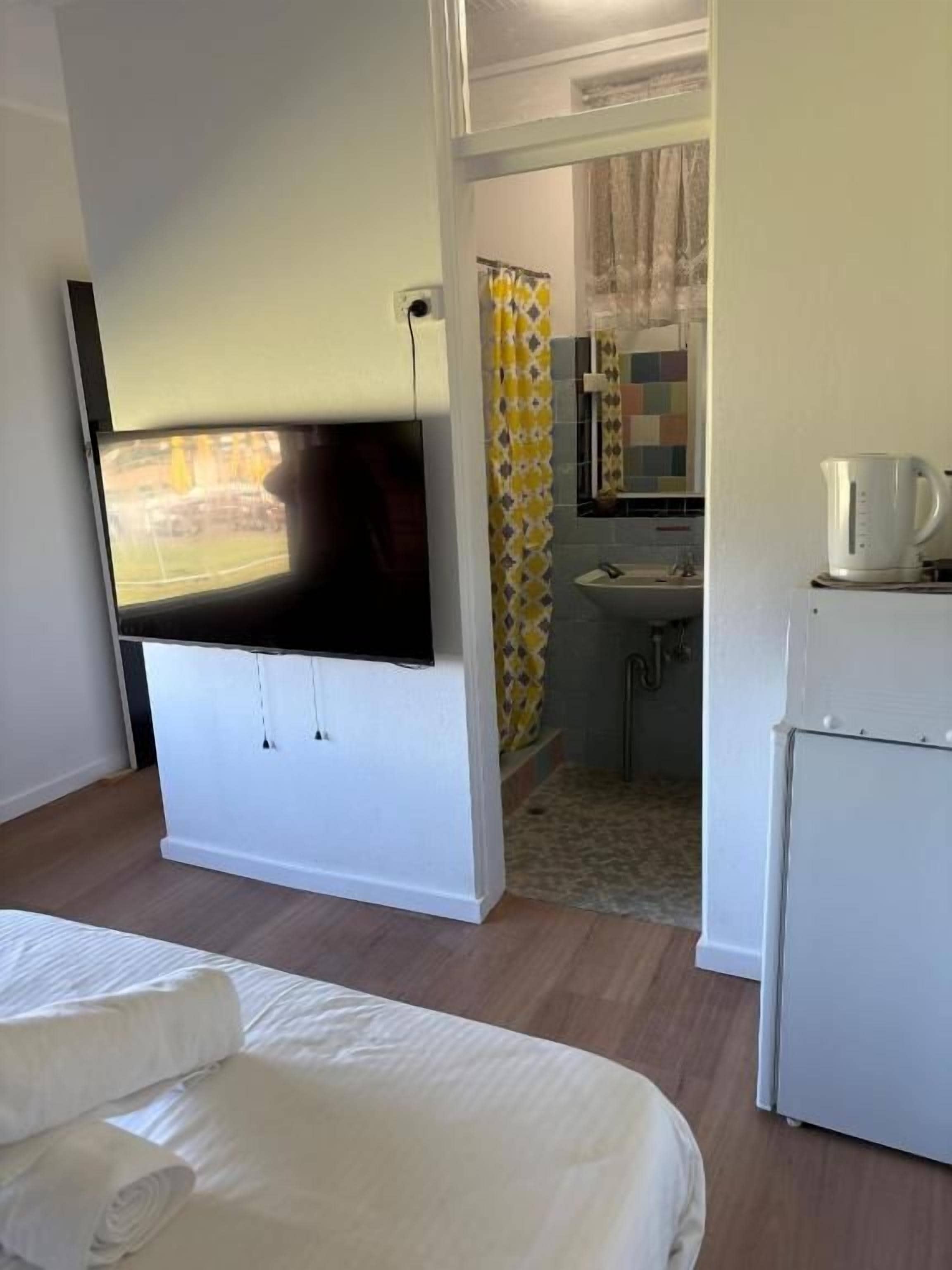 Habitación de hotel con cama, televisión, kitchenette con refrigerador y baño con cortina de ducha.