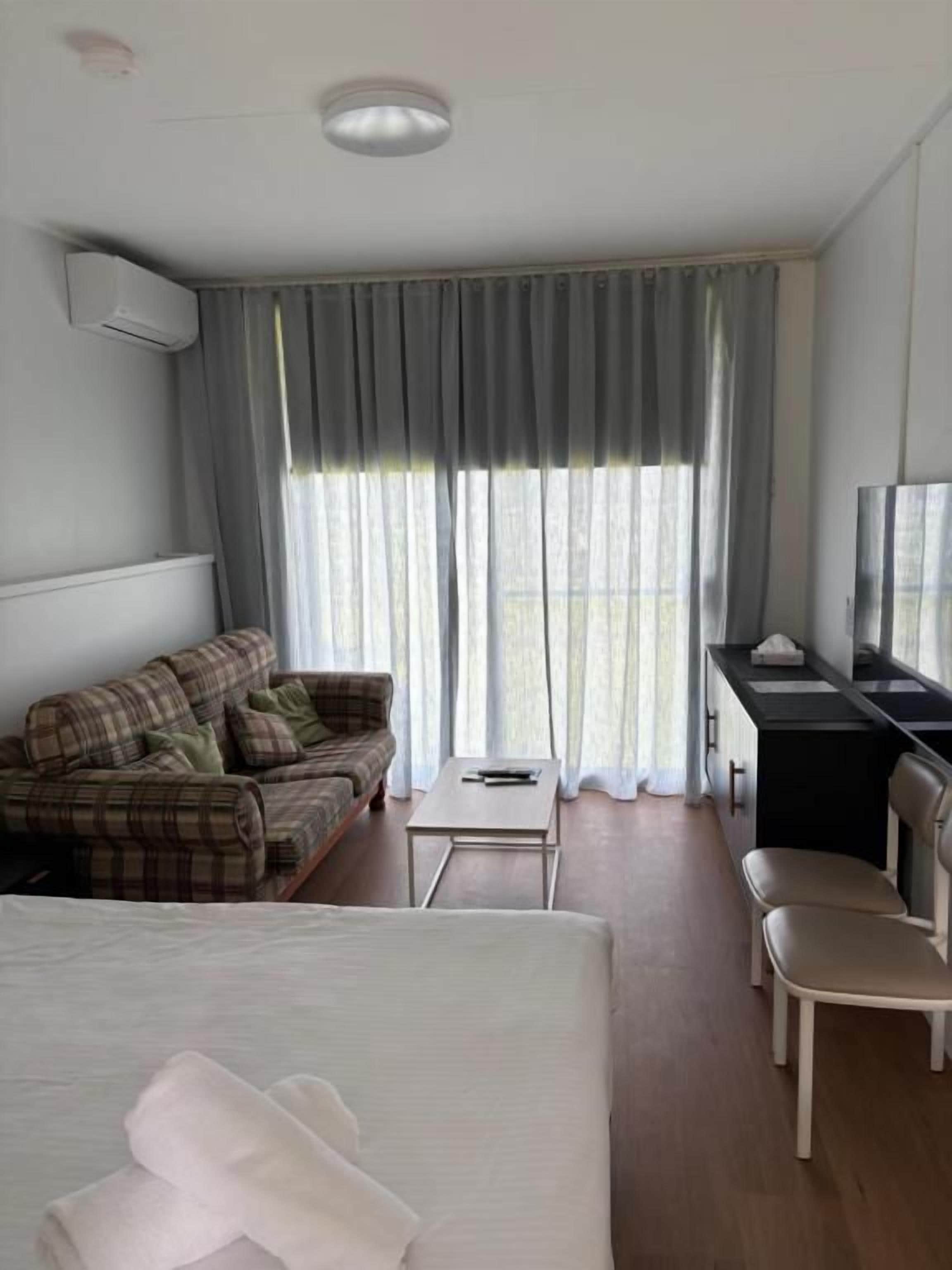 Et hotelværelse med seng, sofa, skrivebord, stol og fjernsyn.