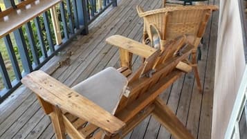 Een houten terras met een tafel met glazen blad en rieten stoelen.