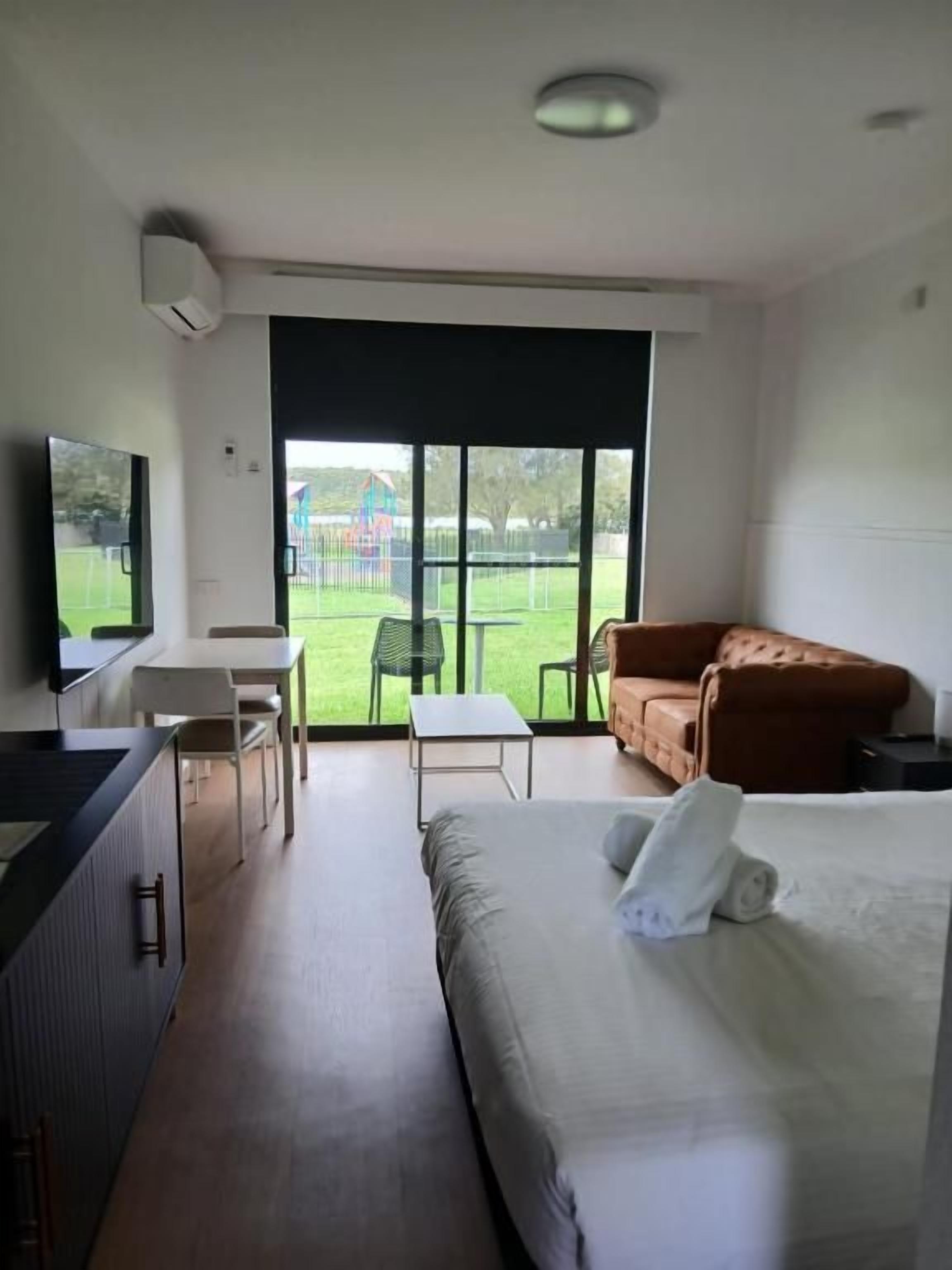 Habitación de hotel con cama, escritorio, silla y vista a un área verde exterior.