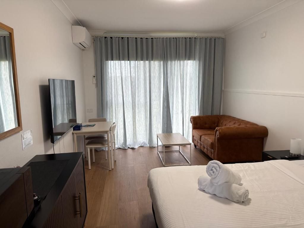 A hotel room with a bed, a desk, a chair, a sofa, and a window with curtains.