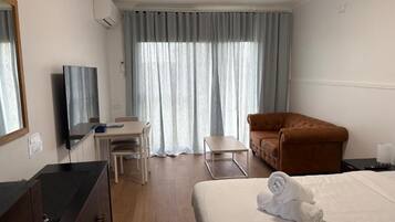 A hotel room with a bed, a desk, a chair, a sofa, and a window with curtains.
