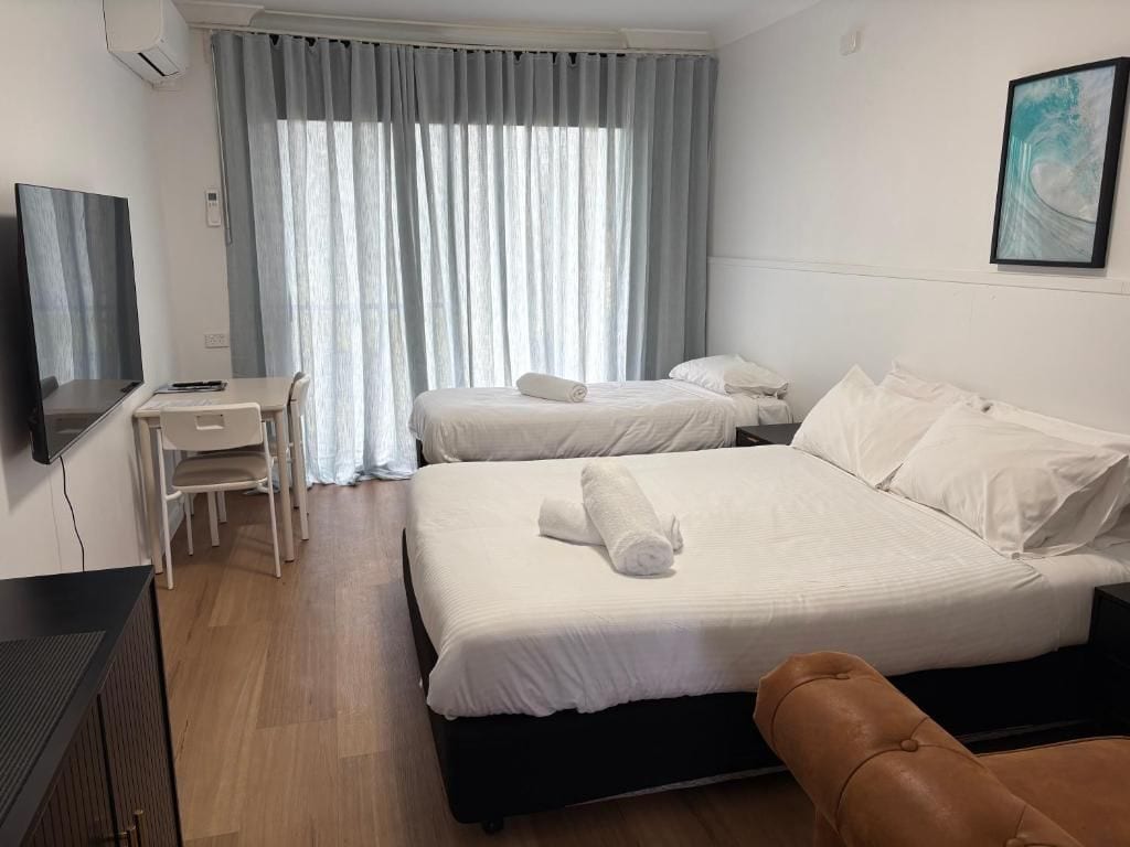 A hotel room with two beds, a desk, a chair, and a TV.
