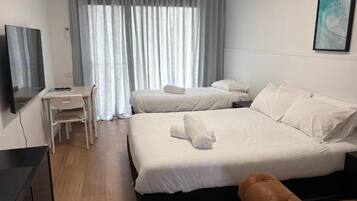 A hotel room with two beds, a desk, a chair, and a TV.