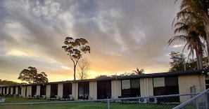 A row of single-story buildings with large windows, likely a hotel or hostel, with a grassy area in front and trees in the background. - Waterview Motel Sussex Inlet (Sussex Inlet)