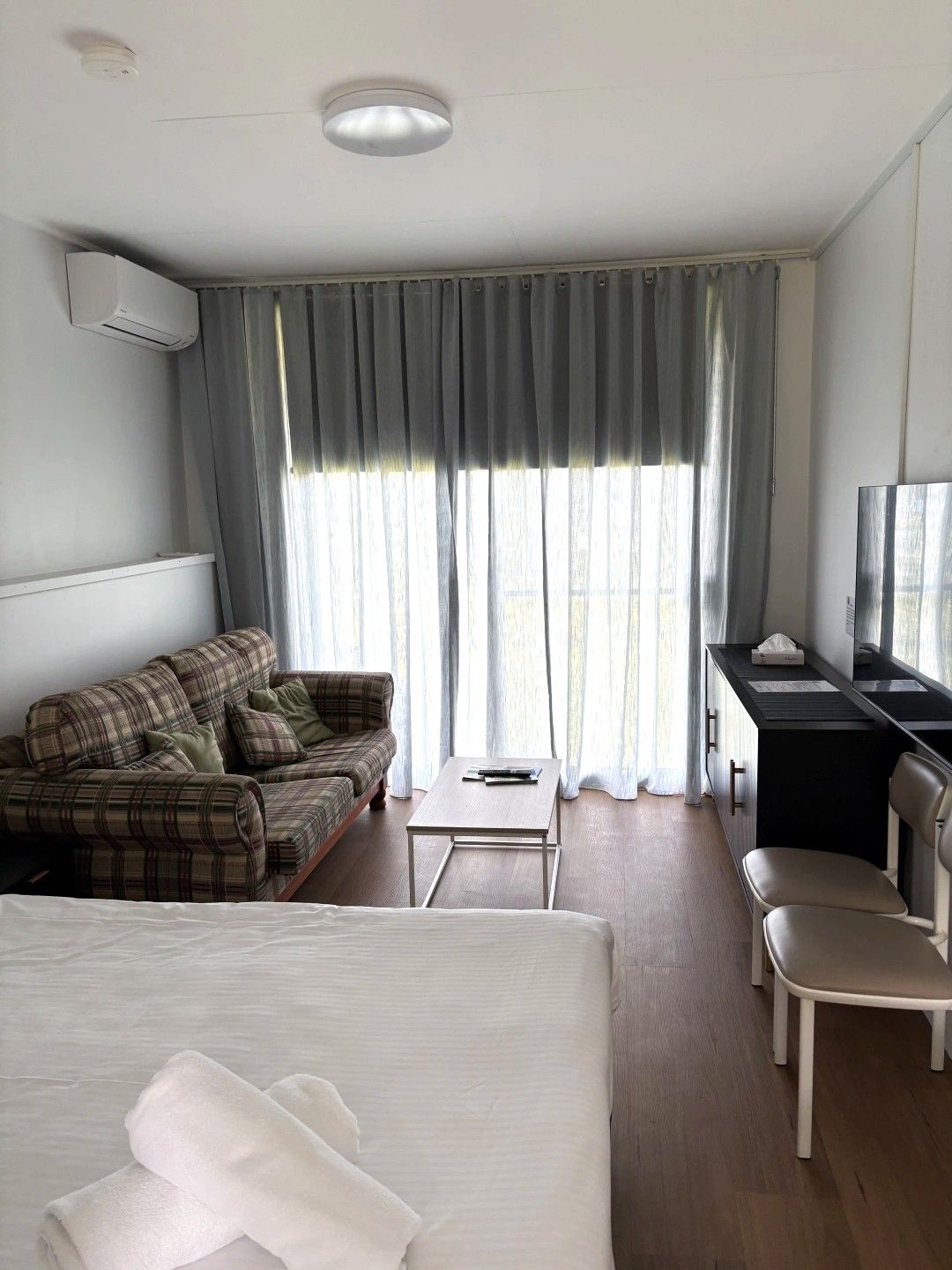 A hotel room with a bed, a sofa, a desk, a chair, and a television.