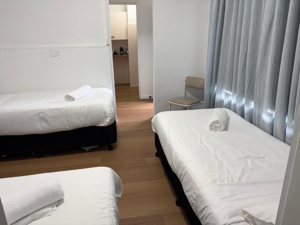 A hotel room with two beds, a chair, and a view of the hallway.