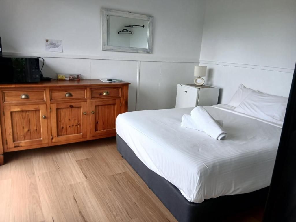Une chambre d’hôtel avec un lit, une commode en bois et un petit placard blanc.