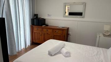 A hotel room with a bed, a wooden dresser, a mirror, and a window with curtains.