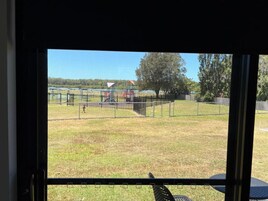 Vista a través de una ventana de un área verde exterior con un parque infantil y un campo deportivo cercado.