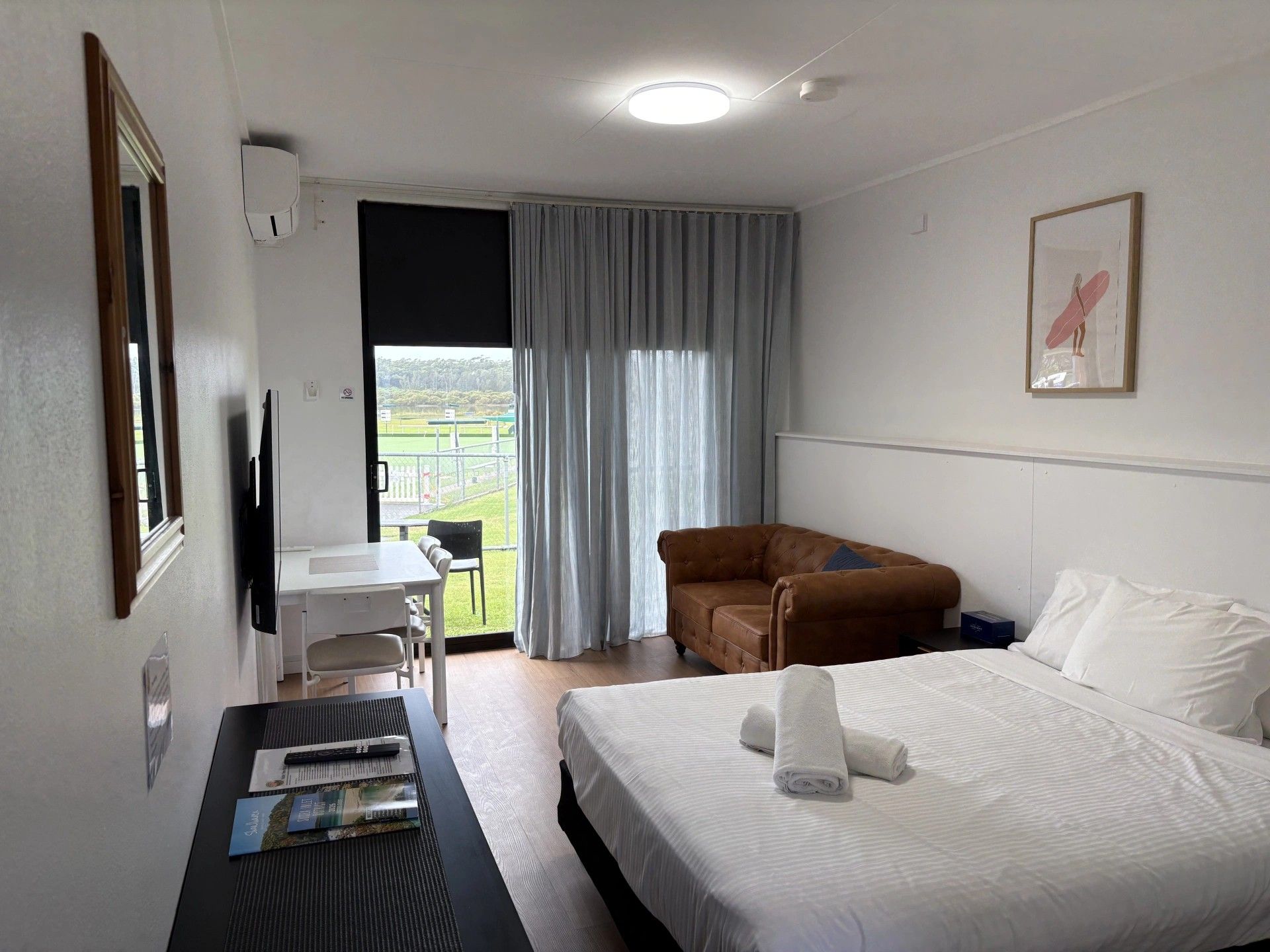 Een hotelkamer met een bed, een bruine bank, een bureau met stoel, een televisie en een raam met gordijnen.