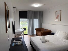 Una habitación de hotel con cama, un sofá marrón, un escritorio con silla, un televisor y una ventana con cortinas.