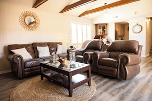 Ein Wohnzimmer mit einem braunen Ledersofa, einem Glastisch und einem braunen Ledersessel.