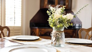 Una mesa de comedor con platos blancos, un florero de vidrio con un adorno de corazón y una silla de madera.