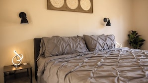 Un dormitorio con cama, lámparas de noche, un adorno en la pared y una mesita de noche.