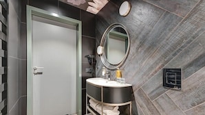 A modern bathroom with a grey tiled wall, a round mirror, a black vanity, and a white door. - Hotel Grano Gdansk SPA & Wellness (Gdańsk)