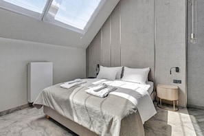 Une chambre moderne avec un puits de lumière, un lit avec des serviettes soigneusement pliées, une table de chevet et un radiateur.