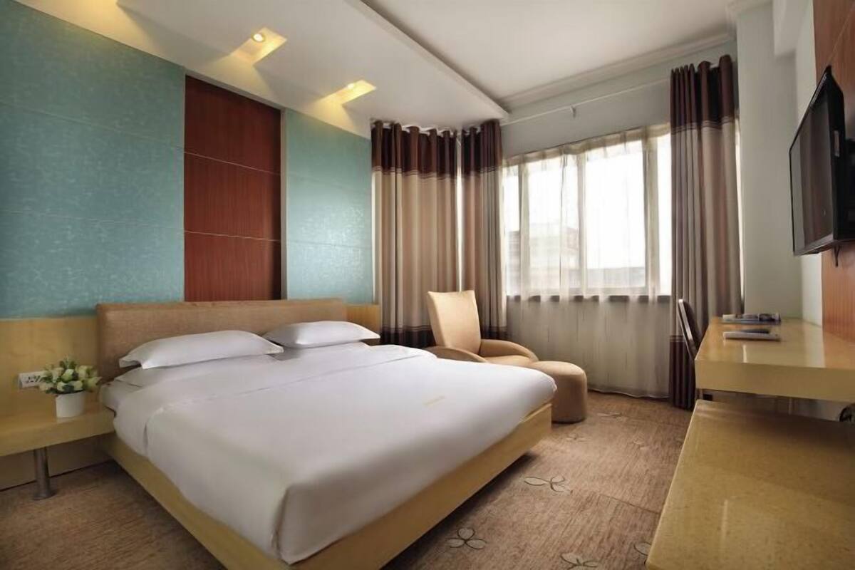 A hotel room with a bed, a chair, a desk, and a television.