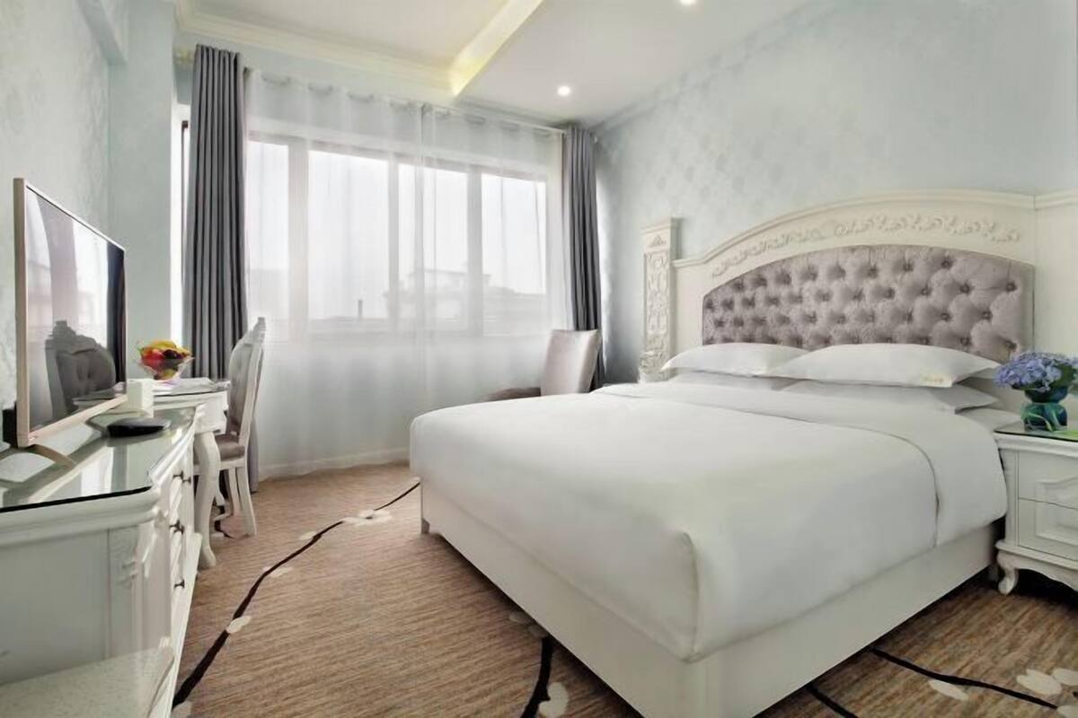 A hotel room with a large bed, a desk with a chair, a television, and a window with curtains.