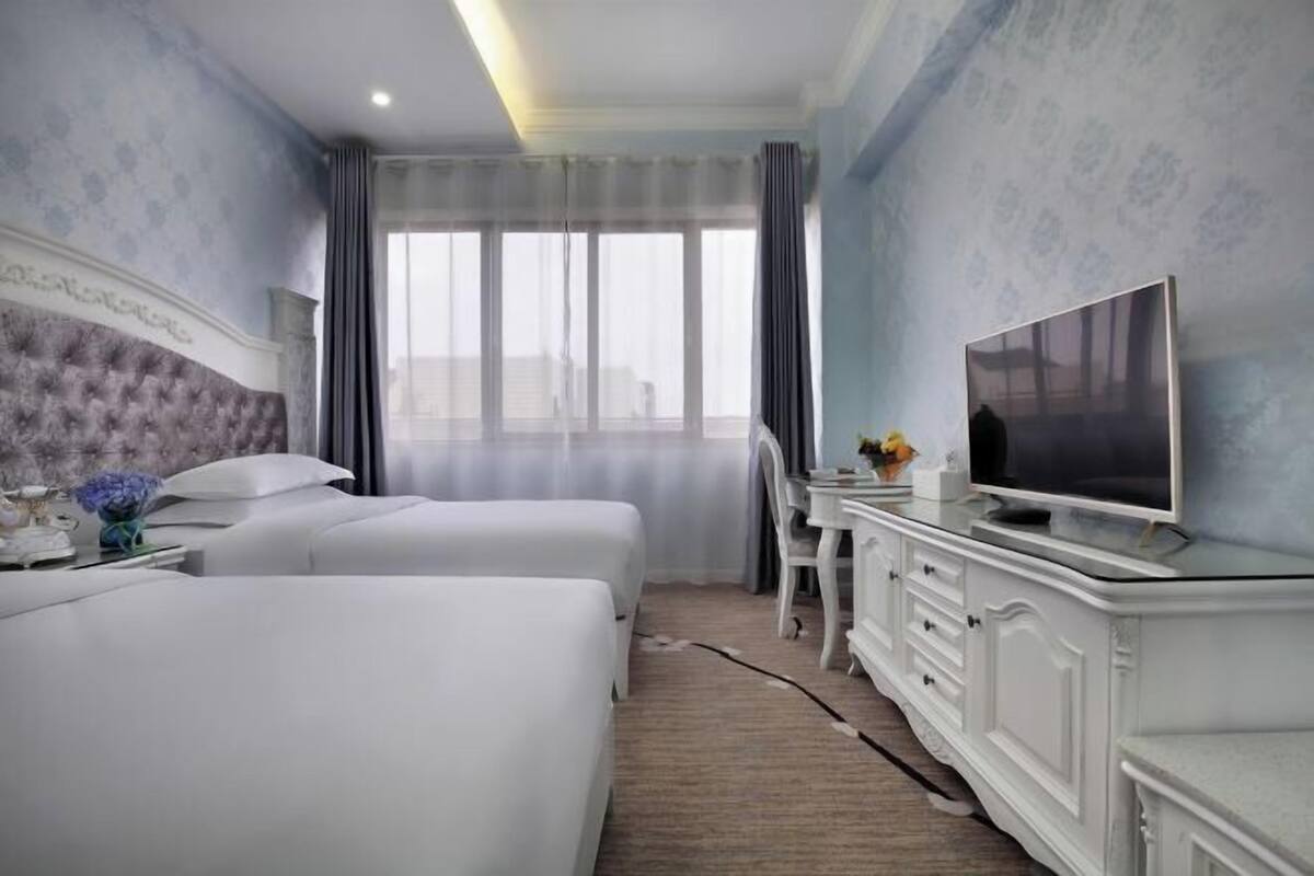 A hotel room with two beds, a desk, a television, and a view of the city.