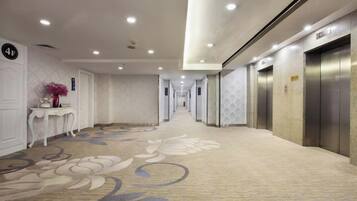 A hotel corridor with carpeted flooring, a reception desk, and elevators.