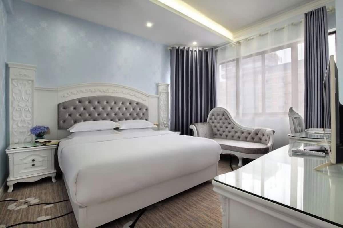 A bedroom with a large bed, a bedside table, a chair, and a desk with a mirror.