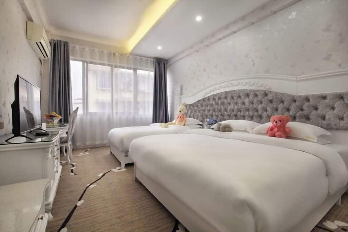 A hotel room with two beds, a TV, a dresser, and a window with curtains.