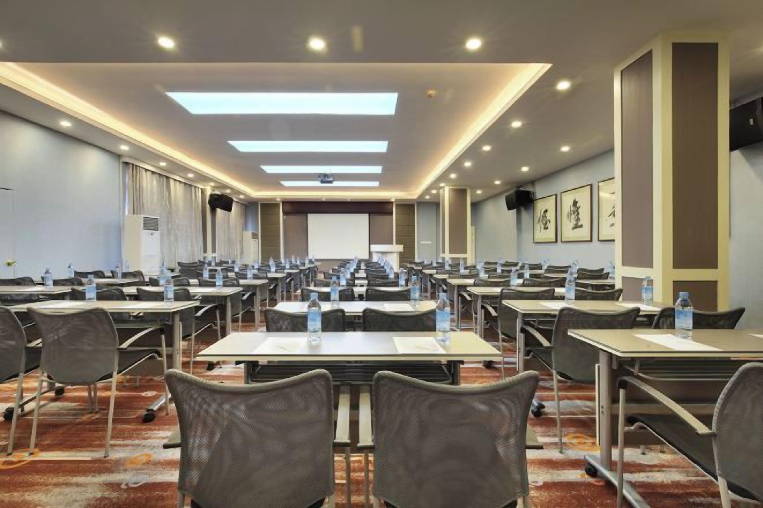A conference room with multiple tables and chairs, equipped with water bottles, and a projection screen at the front.