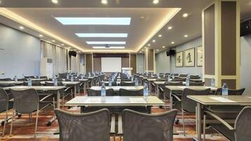 A conference room with multiple tables and chairs, equipped with water bottles, and a projection screen at the front.