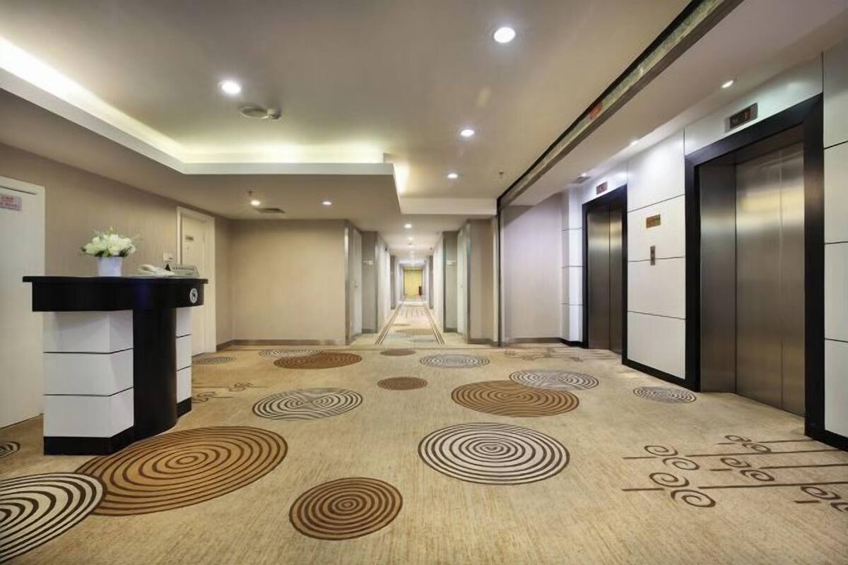 A hotel hallway with a carpeted floor, a reception desk, and two elevators.