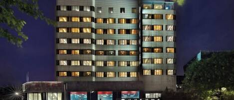A multi-story hotel with a modern facade, multiple balconies, and illuminated windows.