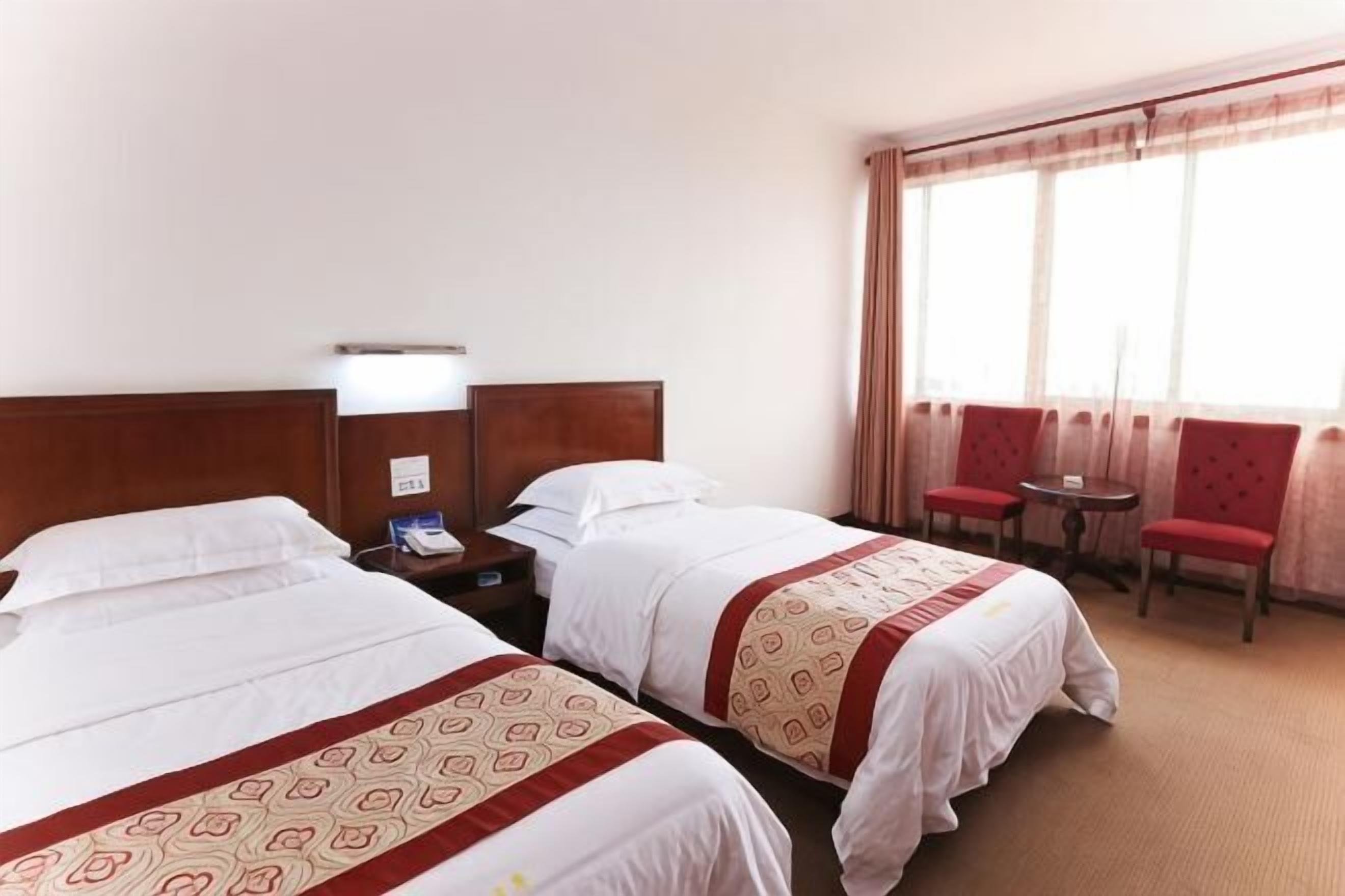 A hotel room with two beds, a small table, two chairs, a nightstand, and a window with curtains.