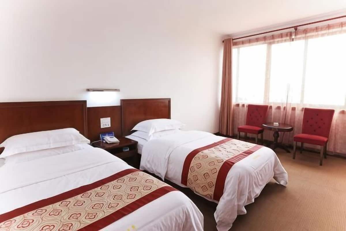 A hotel room with two beds, a small table, two chairs, a nightstand, and a window with curtains.