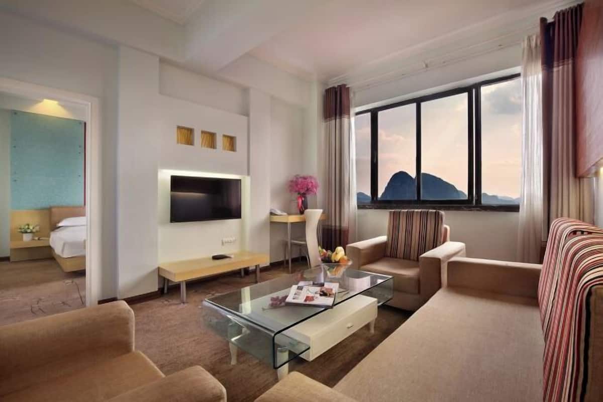 A modern hotel room with a glass coffee table, a sofa, a TV, and a large window with a mountain view.