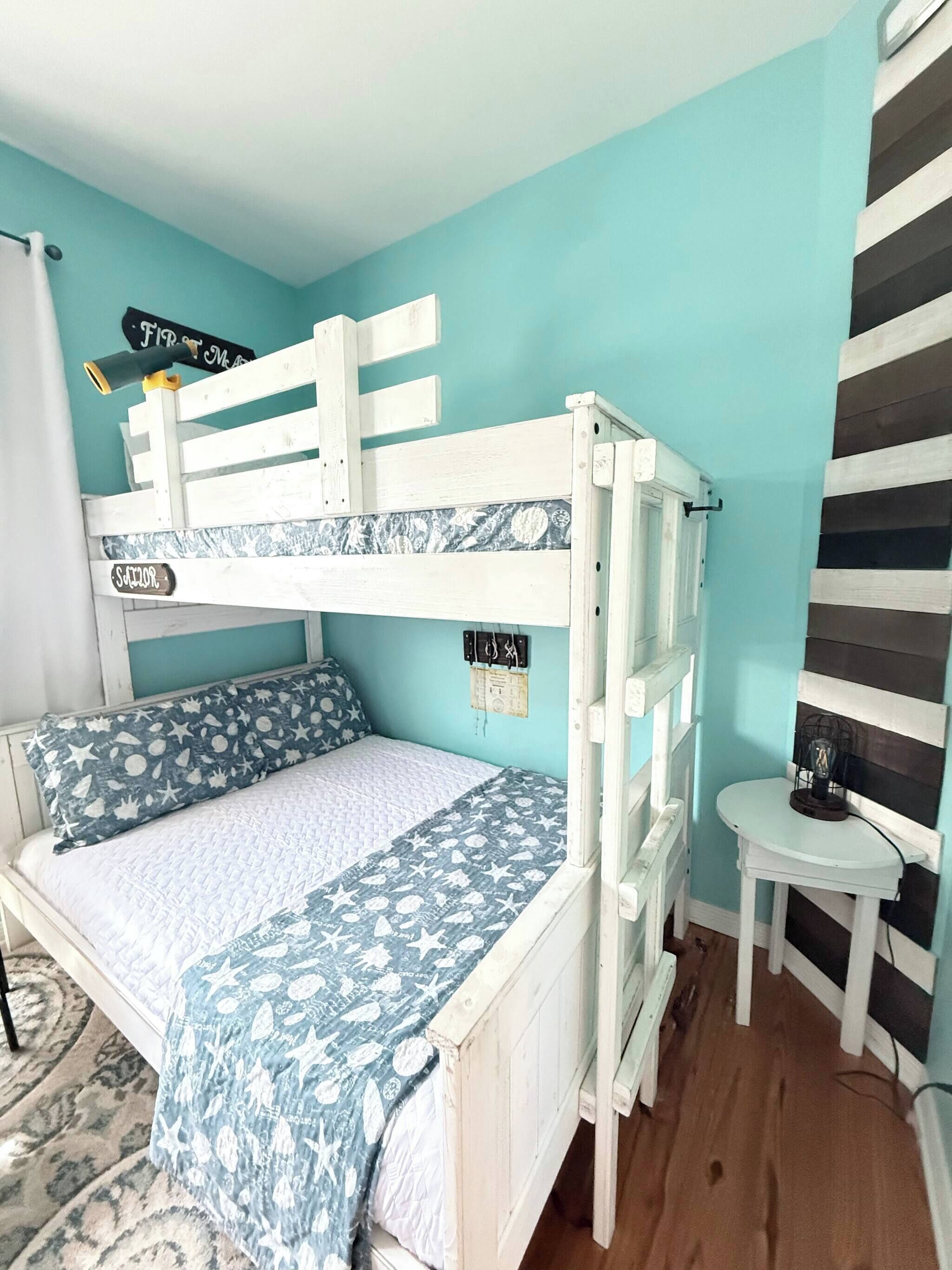 A bunk bed room with a teal wall, a small table, and a decorative sign.
