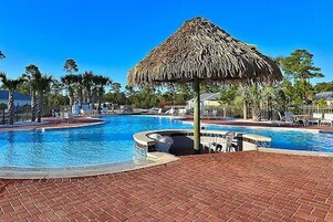 Una piscina con una estructura de techo de paja, rodeada de palmeras y un camino de ladrillo.
