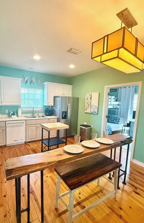 A kitchen with white cabinets, a wooden dining table, and a hanging light fixture. - 2602 Rookery 1 2 A Shiny Penny - Beach hot tub Pool (Gulf Shores)