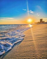Una playa con olas, un atardecer y edificios al fondo.