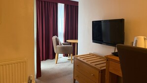 A hotel room with a bed, a TV, a desk, a chair, and a window with curtains. - Executive Single: Comfort for Solo Travellers in Blaby (Blaby)
