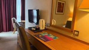 A hotel room with a wooden desk, a television, a coffee maker, a mirror, and a window with curtains. - Executive Single: Comfort for Solo Travellers in Blaby (Blaby)
