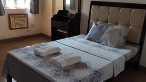 A neatly made bed with a patterned bedspread, two pillows, and two folded towels on the bed. - ValueNest Stay (Naga)