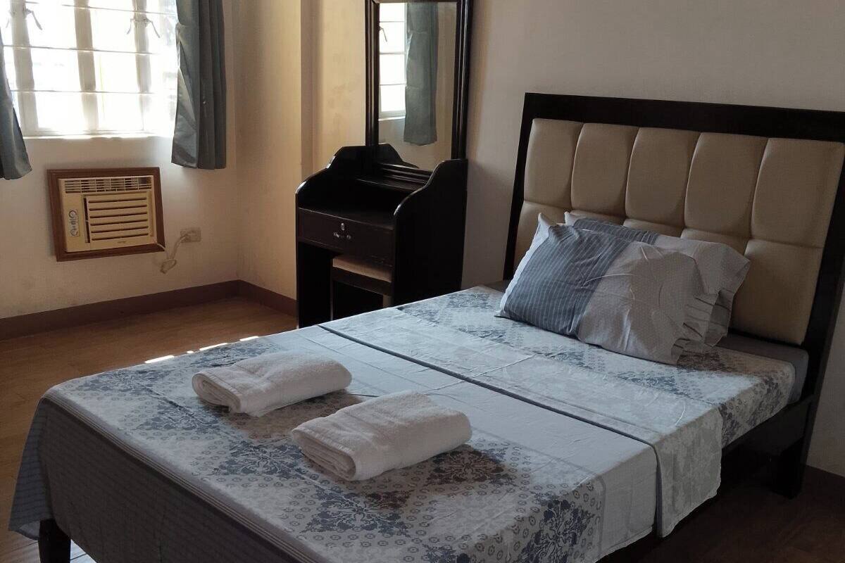 A neatly made bed with a patterned bedspread, two pillows, and two folded towels on the bed.