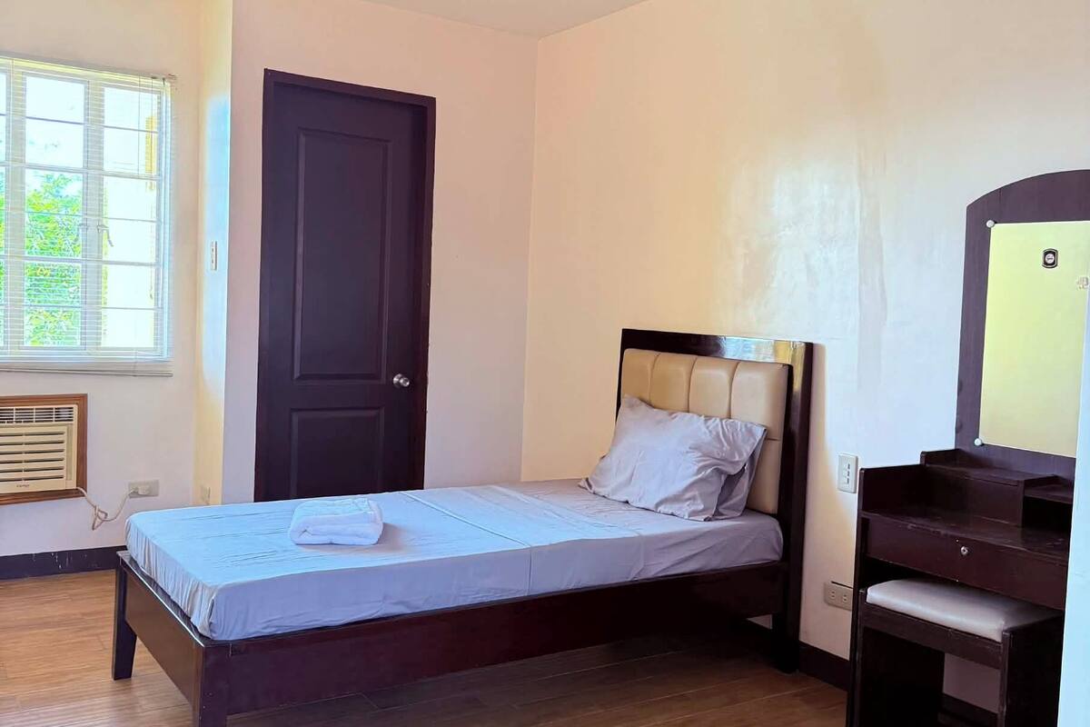A bedroom with a bed, a door, a window, and a desk.